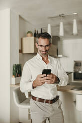 Smiling businessman using mobile phone at home - DMGF00818