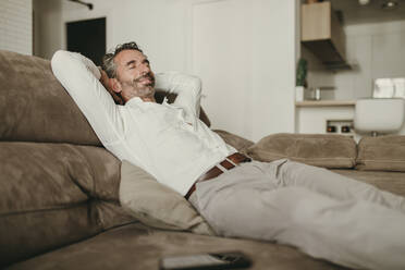 Smiling businessman relaxing on sofa at home - DMGF00830