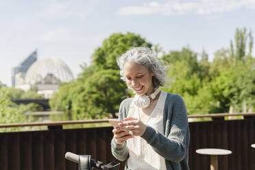 Lächelnde Frau mit Mobiltelefon an einem sonnigen Tag - SEAF01047