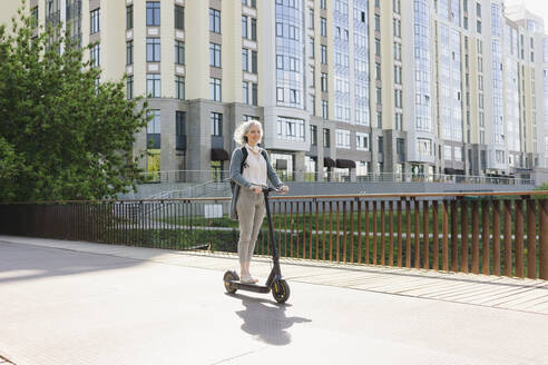 Woman riding electric push scooter at street on sunny day - SEAF01048