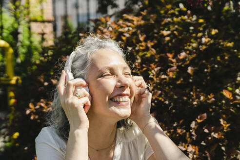 Glückliche Frau, die drahtlose Kopfhörer im Park einstellt - SEAF01066
