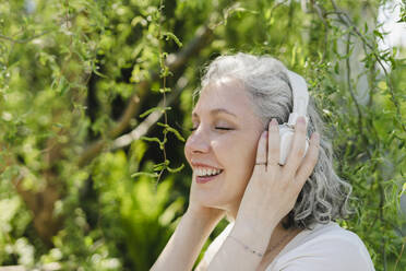 Happy woman enjoying music through wireless headphones in park - SEAF01085