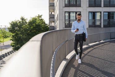 Junger Geschäftsmann mit Smartphone auf einer Fußgängerbrücke - DIGF18305