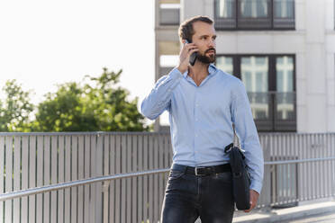 Junger Geschäftsmann spricht mit seinem Smartphone vor einem Gebäude - DIGF18307