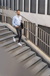 Young businessman with bag walking on steps - DIGF18309