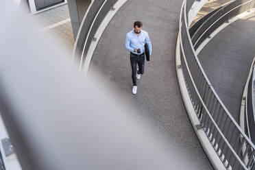 Junger Geschäftsmann mit Mobiltelefon auf einer Fußgängerbrücke - DIGF18311