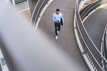 Young businessman using mobile phone walking on footbridge - DIGF18311