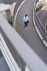 Businessman using smart phone walking on footbridge - DIGF18312