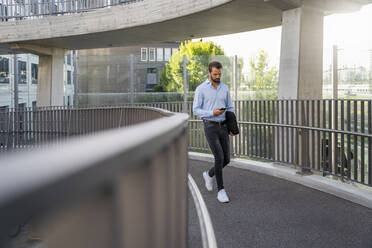 Junger Geschäftsmann benutzt Mobiltelefon an einer Fußgängerbrücke - DIGF18316