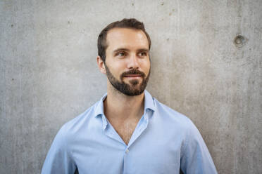 Smiling young businessman standing in front of wall - DIGF18325