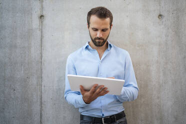 Businessman using tablet PC standing in front of wall - DIGF18335