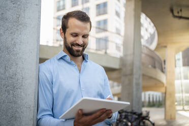 Lächelnder junger Geschäftsmann mit Tablet-PC unter einer Brücke stehend - DIGF18343