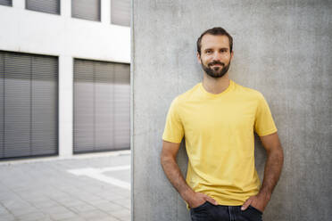 Smiling young man with hands in pocket leaning on wall - DIGF18363