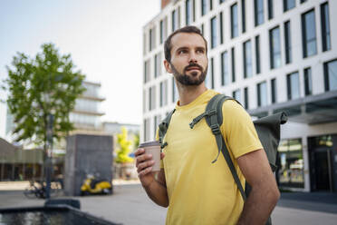 Young man with disposable coffee cup standing outside building - DIGF18366