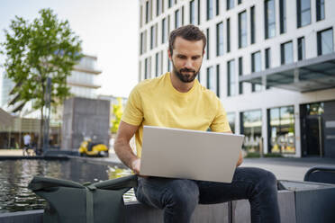 Freelancer using laptop sitting in front of pond - DIGF18367