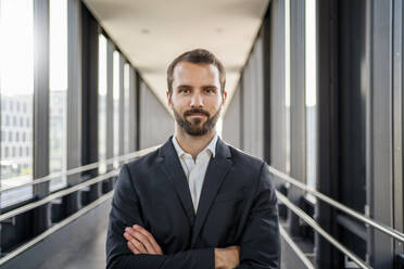 Confident young businessman standing with arms crossed on elevated walkway - DIGF18378