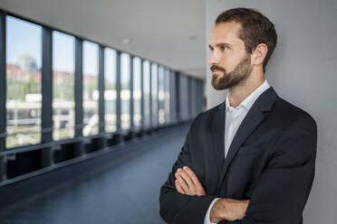 Contemplative businessman with arms crossed standing in front of wall - DIGF18382