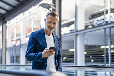 Businessman using smart phone standing on escalator - DIGF18388