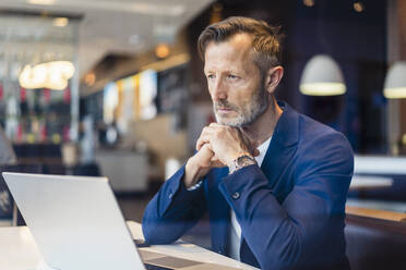 Contemplative businessman with laptop in cafe - DIGF18397