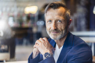 Smiling mature businessman with hands clasped in cafe - DIGF18402