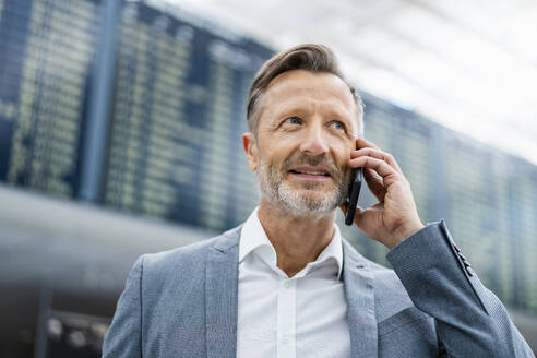 Lächelnder reifer Geschäftsmann im Gespräch mit einem Smartphone - DIGF18428