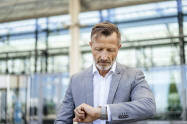 Mature businessman checking time on wristwatch - DIGF18437