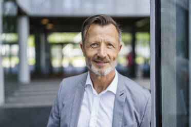 Smiling mature businessman leaning on wall - DIGF18439