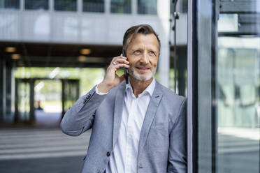 Smiling mature businessman talking on mobile phone leaning on wall - DIGF18445