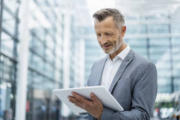 Lächelnder Geschäftsmann in grauem Blazer mit digitalem Tablet - DIGF18450