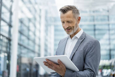 Smiling businessman in gray blazer using digital tablet - DIGF18450