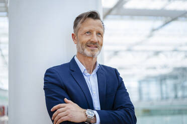 Smiling mature businessman with arms crossed in front of column - DIGF18458