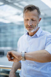 Älterer Geschäftsmann, der die Zeit auf seiner Armbanduhr überprüft - DIGF18463