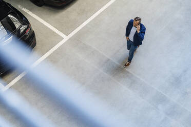 Businessman talking on smart phone walking in parking lot - DIGF18467