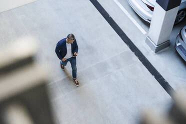 Businessman using mobile phone walking in parking lot - DIGF18469