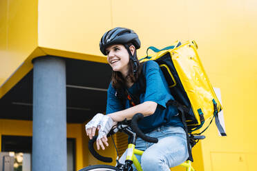 Glückliche Lieferfrau mit Rucksack auf dem Fahrrad sitzend - DAMF01040