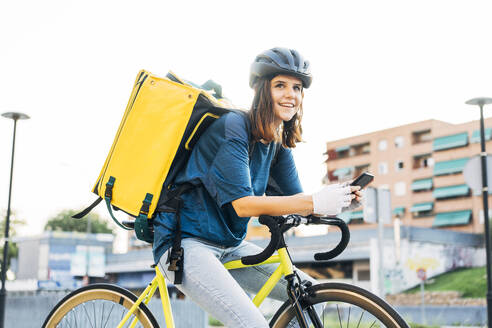 Smiling delivery person with mobile phone sitting on bicycle - DAMF01056