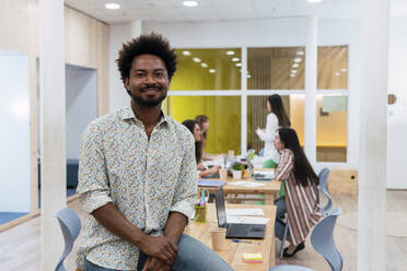 Portrait of confident businessman in office with colleagues in background - PNAF04143