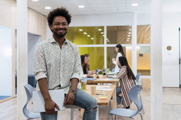 Portrait of smiling businessman in office with colleagues in background - PNAF04145