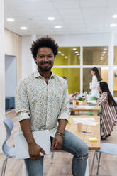 Portrait of smiling businessman in office with colleagues in background - PNAF04146