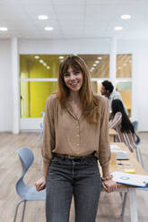 Portrait of smiling businesswoman in office with colleagues in background - PNAF04162