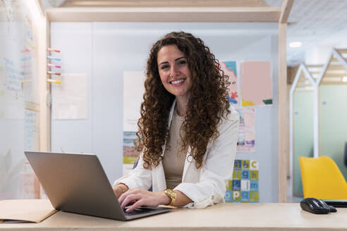 Porträt einer lächelnden brünetten Geschäftsfrau mit Laptop im Büro - PNAF04193