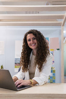 Porträt einer lächelnden brünetten Geschäftsfrau mit Laptop im Büro - PNAF04194