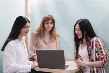 Drei Geschäftsfrauen mit Laptop bei einer Besprechung im Büro - PNAF04252