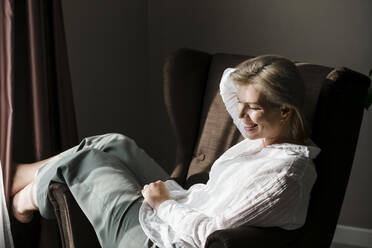Happy woman relaxing in chair at home - LLUF00748
