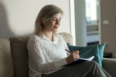 Smiling mature woman writing in diary at home - LLUF00757
