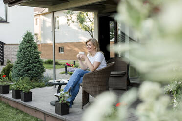 Smiling woman having coffee on porch - LLUF00764