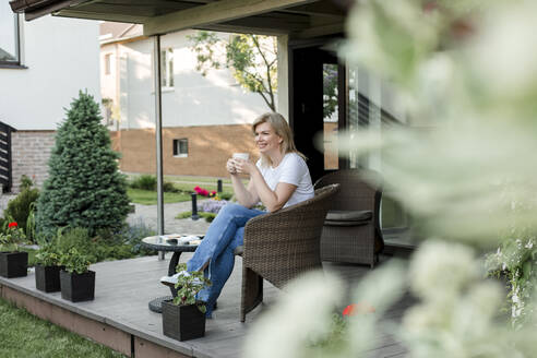 Lächelnde Frau beim Kaffee auf der Veranda - LLUF00764