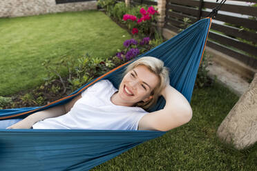 Happy mature woman lying on hammock in garden - LLUF00768