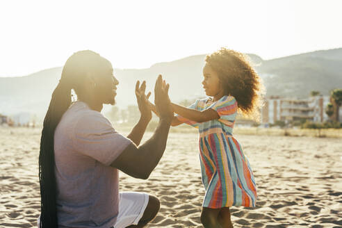 Lächelnder Mann spielt mit seiner Tochter am Strand ein Klatschspiel - OIPF02119
