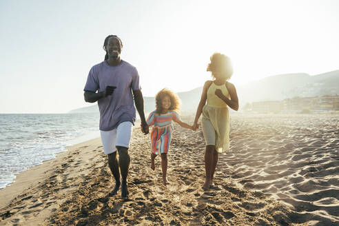 Glückliches Mädchen hält Vater und Schwester an der Hand und läuft am Strand - OIPF02127